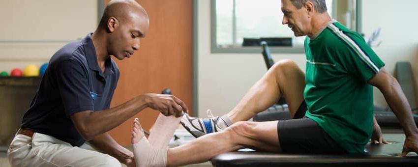 A physical therapist assistant student works in a lab bandaging a patients ankle.